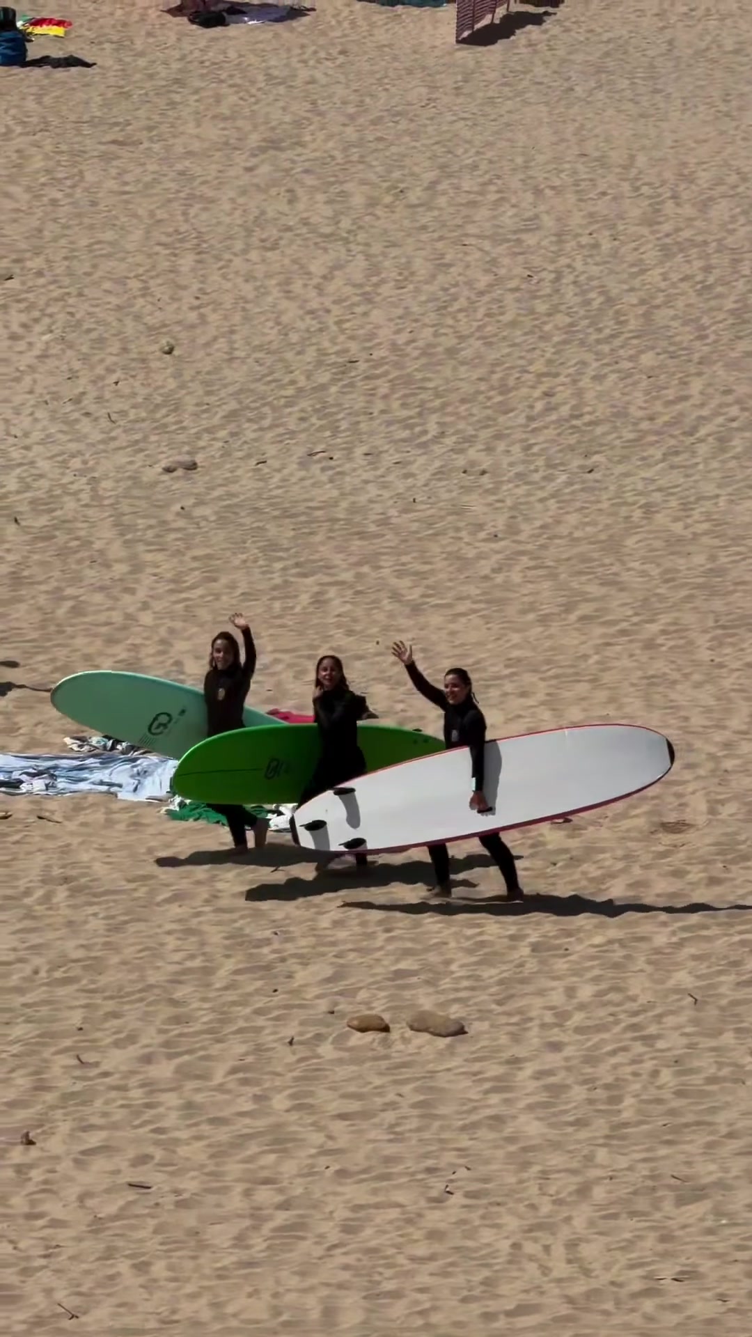 Trois participantes en combinaison avec leurs planches de surf sur une plage au Portugal